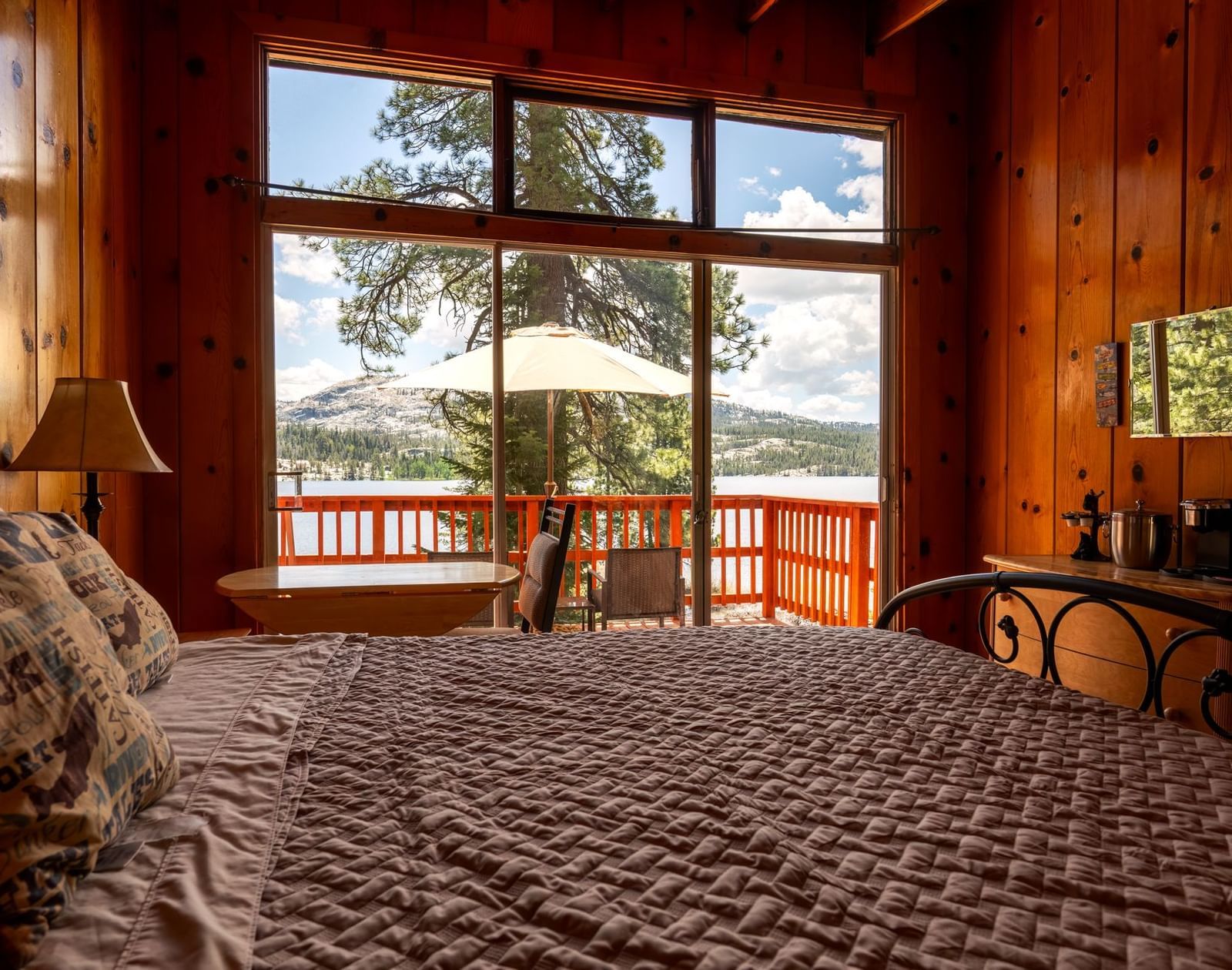 Bedroom with rich wood walls, large windows, and mountain views from a queen bed at Kit Carson Lodge.