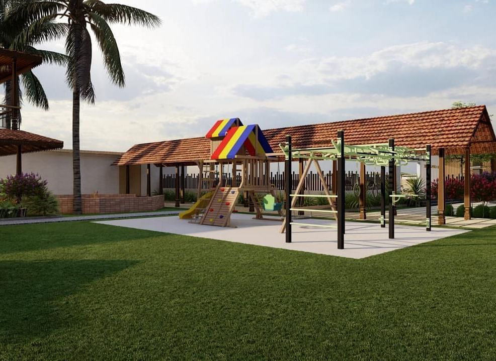 A grassy outdoor area with playground equipment and a building with a brown roof in the background, surrounded by trees and foliage.