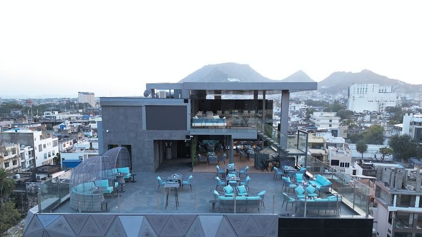 A long shot view of a rooftop restaurant with neatly arranged tables and chairs, offering a scenic backdrop of mountains at Clarks Collection Grand Sapphire, Ajmer.