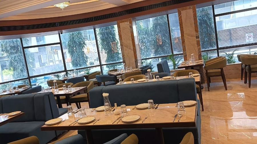 Dining space enclosed with glass, featuring tables and chairs at Hotel Mumbai House, Vashi.