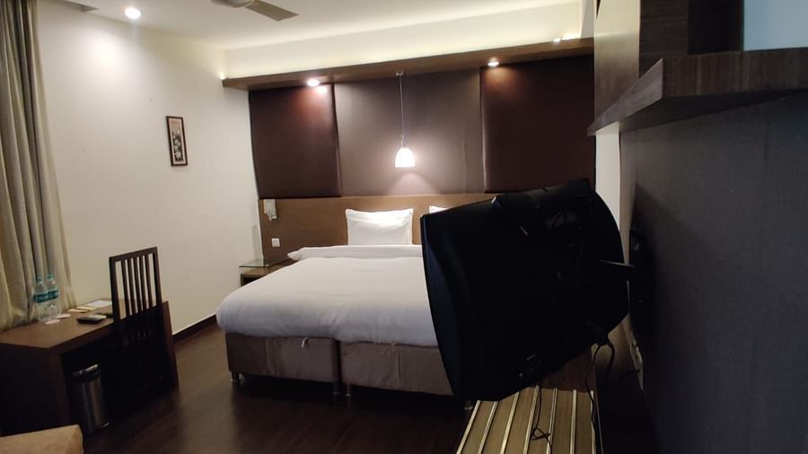 A hotel room with a white bed, a dark wooden wall, and a mounted television - VITS Gurugram