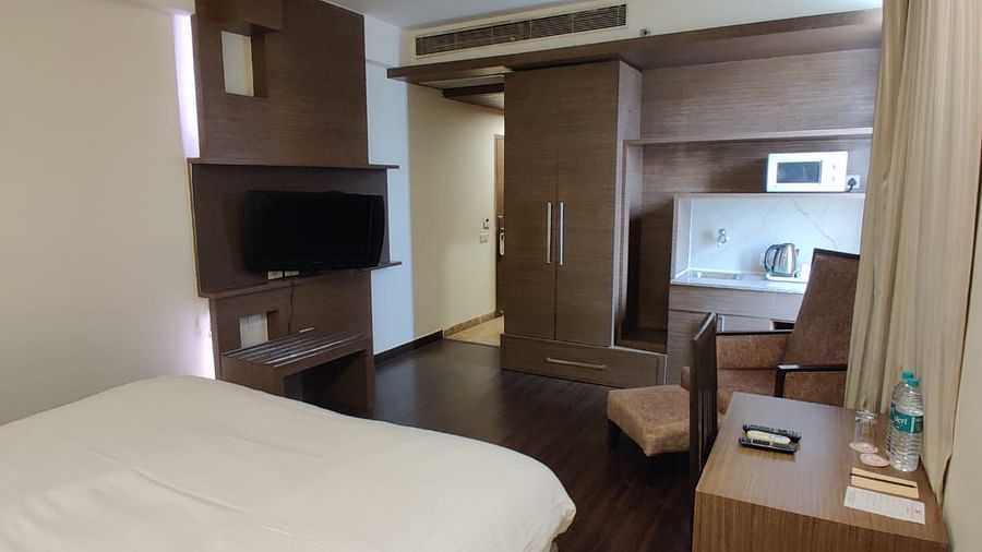 A close-up of a white bed in a hotel room, with a partially visible wardrobe and television - VITS Gurugram