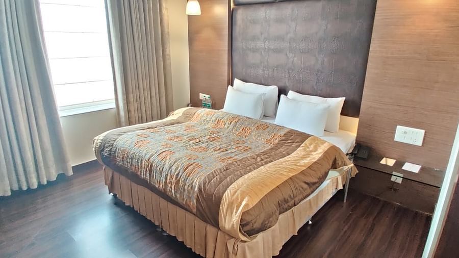 A bedroom with a neatly made bed, decorative pillows, and a window with curtains, creating a comfortable space - VITS Gurugram