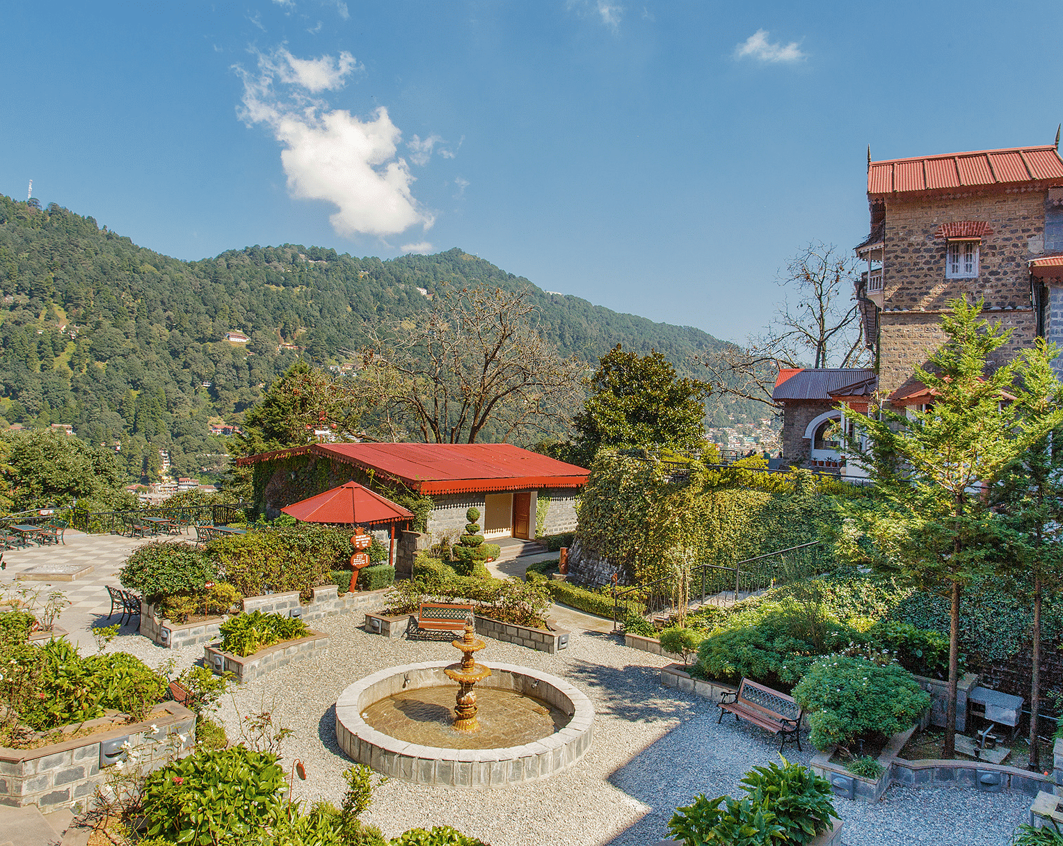 An image of the  garden with a fountain in the middle, with roofs of cottages visible, with a backdrop of the mountains.