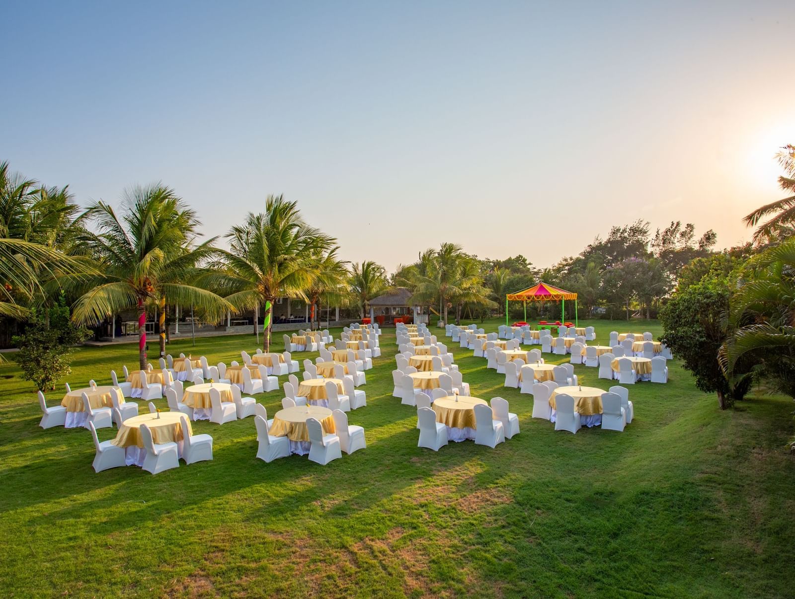 An outdoor event space on a green lawn with numerous round tables and chairs, set up for a gathering under a bright sky with palm trees | Grande Pavillion | Grand Bay Resort and Spa