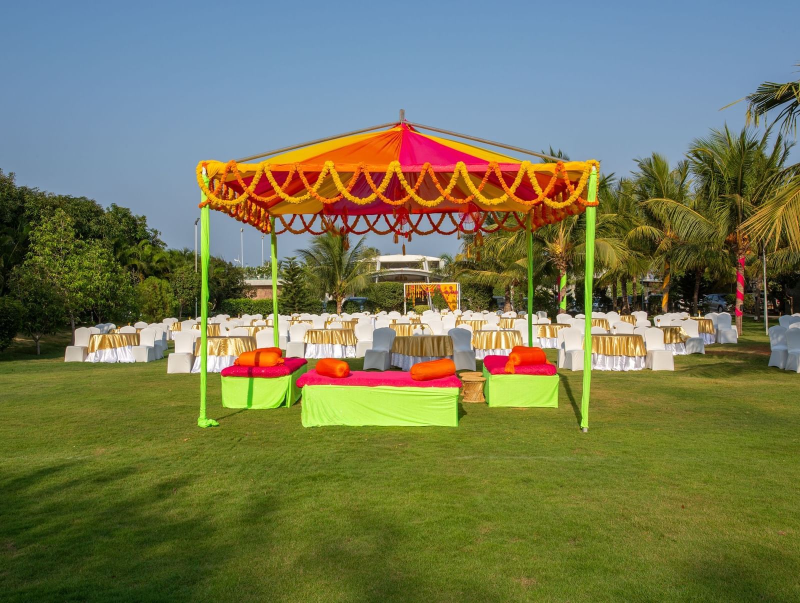 A colorful outdoor event setup featuring an orange and yellow tent, vibrant green and pink seating, and round tables on a manicured lawn | Grande Pavillion | Grand Bay Resort and Spa