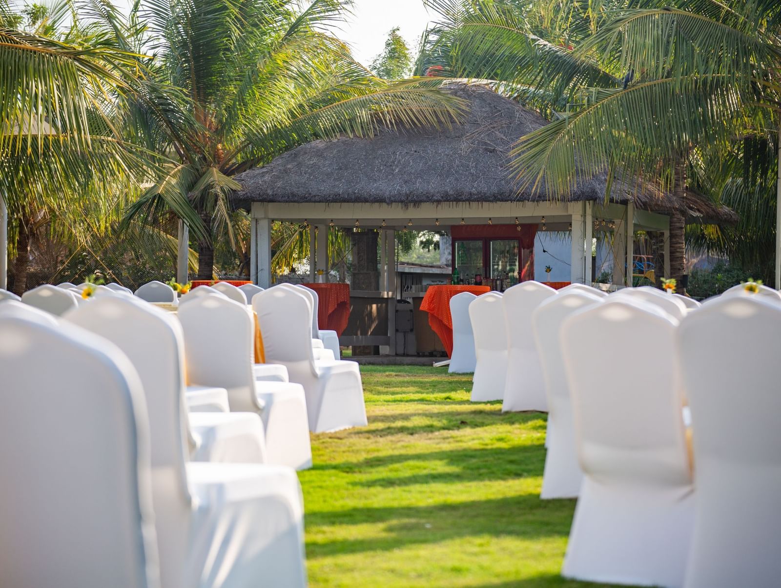 An outdoor event space on a grassy lawn with white chair covers on numerous chairs, under the shade of palm trees  | Citrus Garden | Grand Bay Resort and Spa