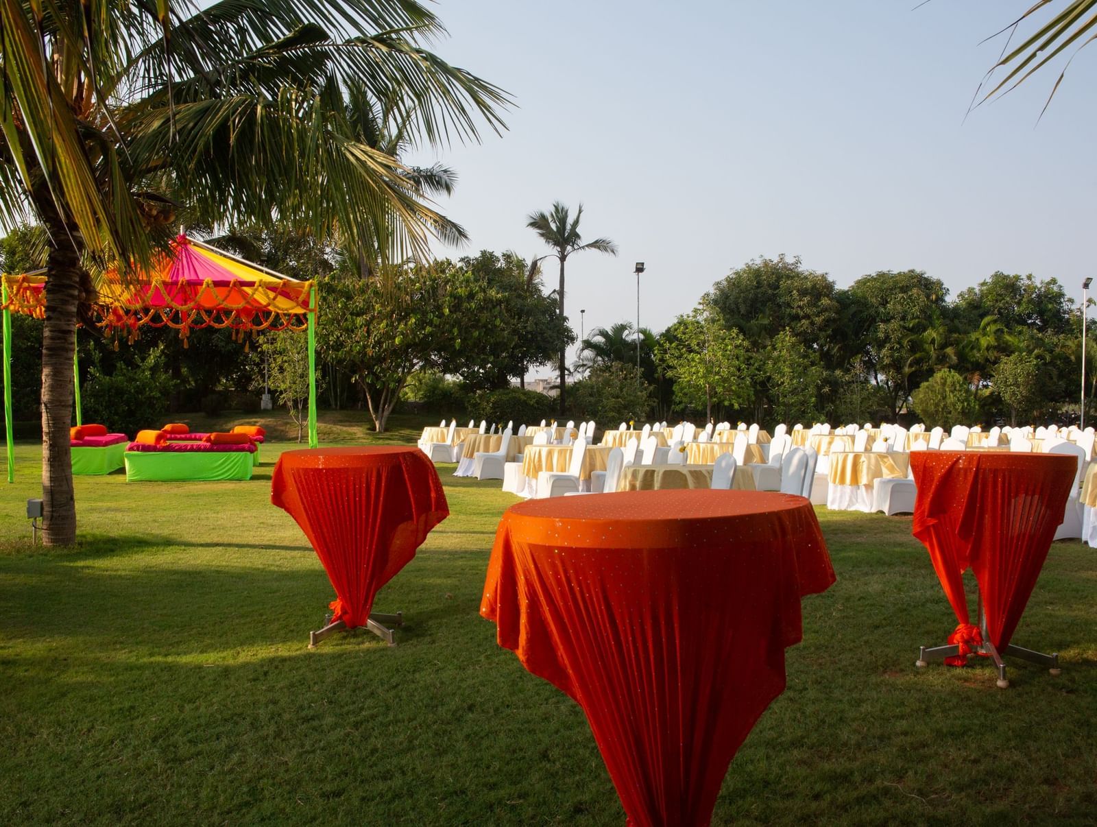 An outdoor gathering on a green lawn with tall orange cocktail tables and chairs, under the shade of palm trees | Citrus Garden | Grand Bay Resort and Spa