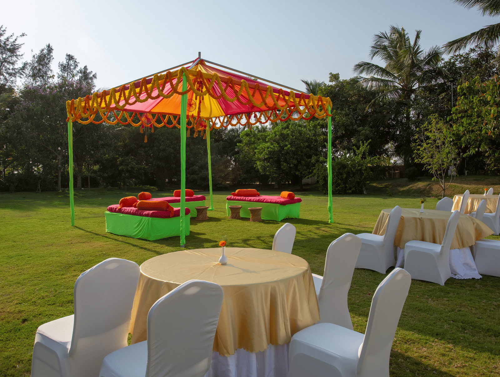 An outdoor yellow and orange tent hosting green and red seating, and round tables on a vibrant green lawn - Grande Bay Resort & Spa, Mamallapuram