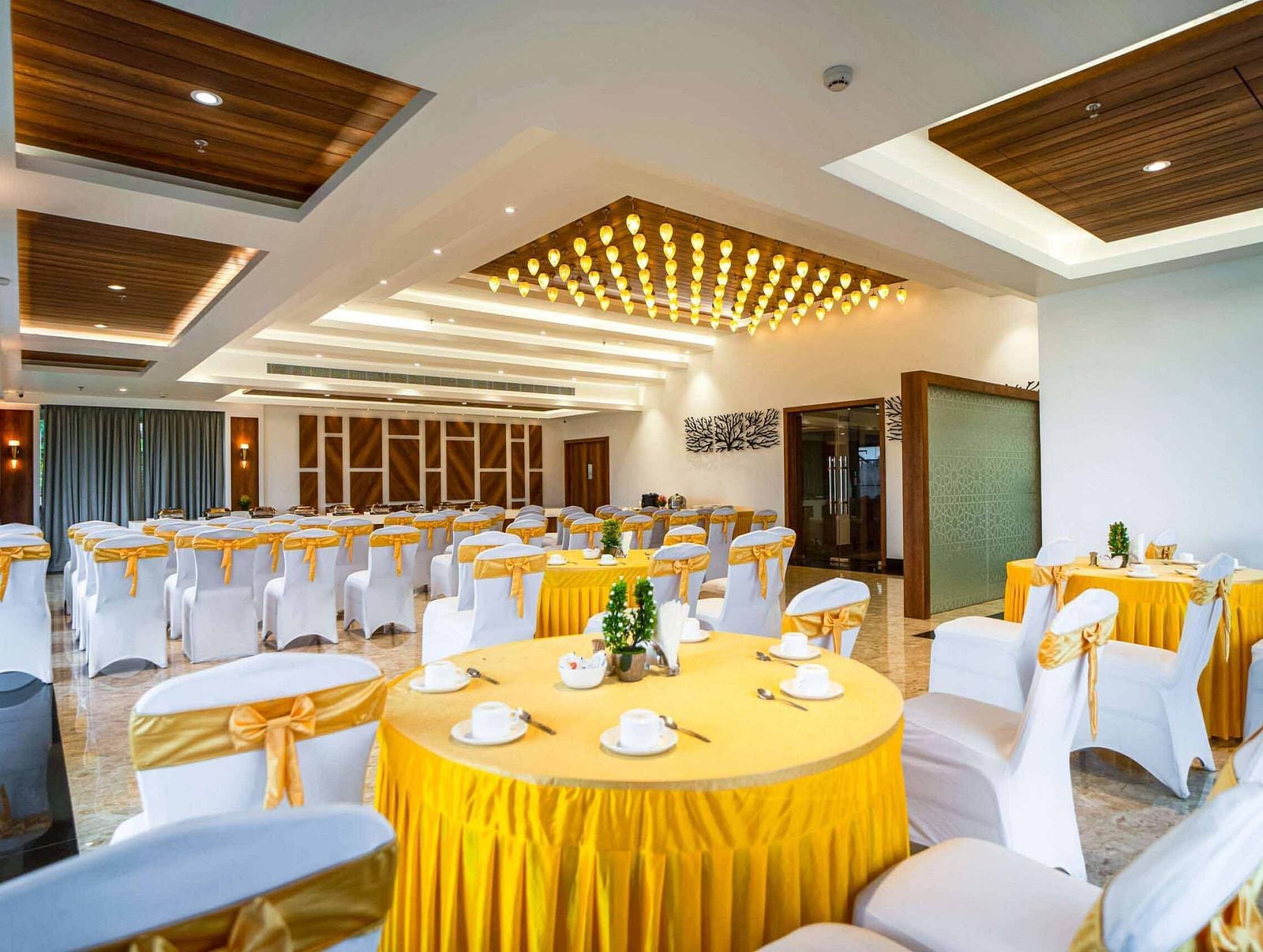A brightly lit banquet hall at Mansha Palace is elegantly prepared for an event with round tables and draped chairs.