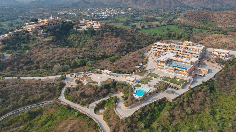 Aerial view of Fateh Vilas, Udaipur, perched on a hilltop with swimming pools, landscaped gardens, and the surrounding Aravalli Hills