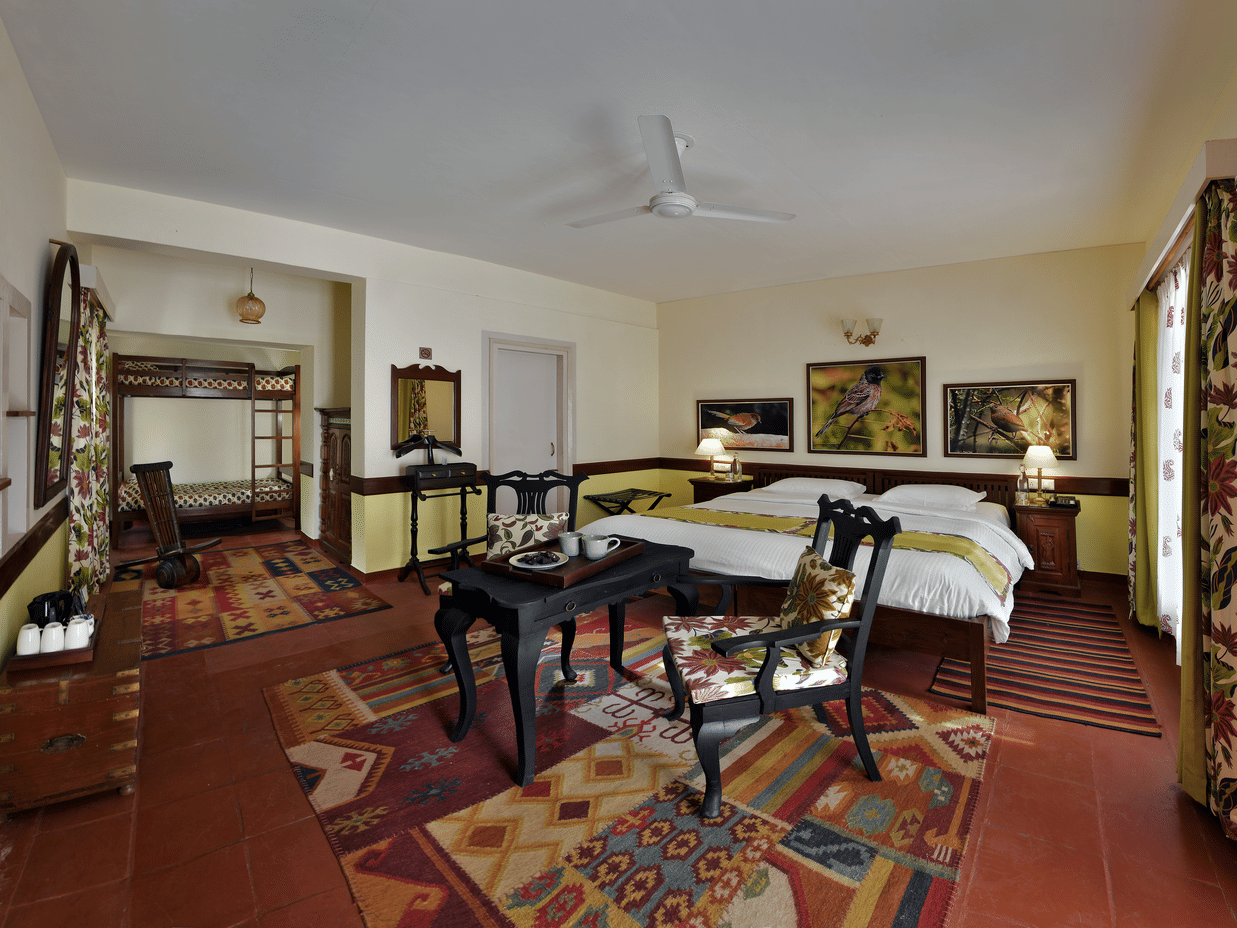Generous bedroom featuring multiple beds wooden furniture patterned rugs and open layout providing convenience at Neemrana’s Glasshouse on The Ganges for families or group travellers.