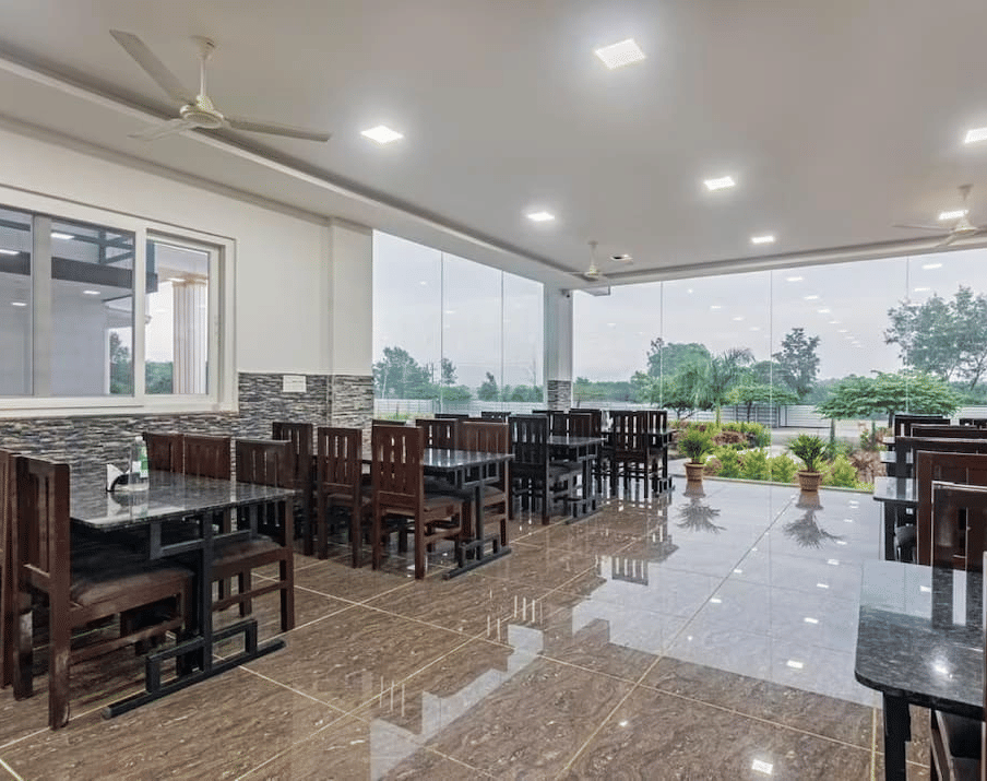 Well-lit restaurant with large windows offering scenic views and comfortable wooden seating at Siri Ambari Resorts and Spa.