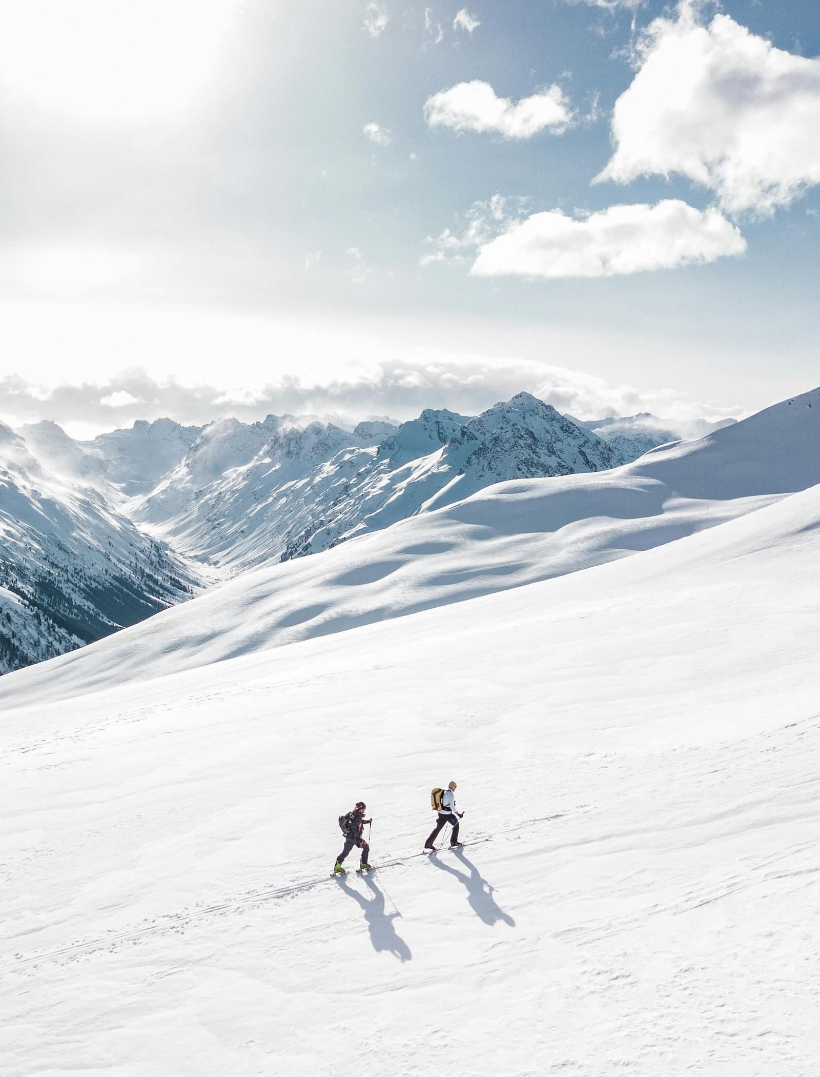 Two people trekking up a snowy mountain during the day.