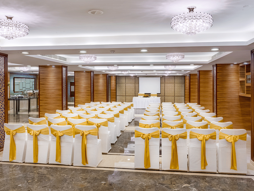 A view from behind of Regency 1 Hall, one of the best Banquet Halls in Park Street, with theatre style seating, a stage at the far end and many chandeliers on the ceiling at Kenilworth Hotel, Kolkata.