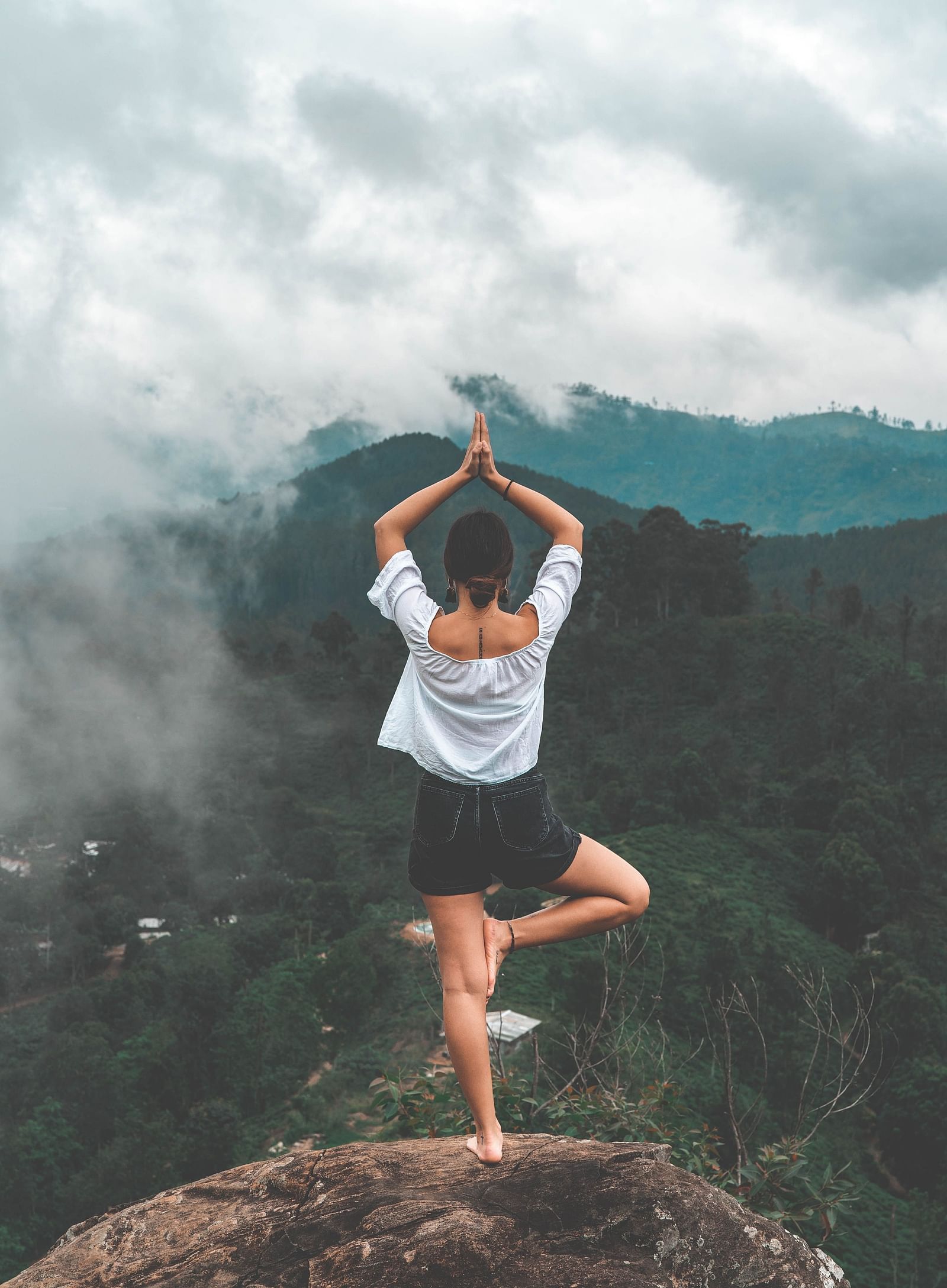 A woman in Vrksasana yoga pose amidst the mountains during daytime