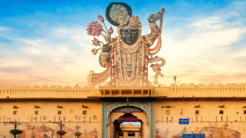 Wide view of a traditional structure in Nathdwara topped with a large statue of Lord Krishna under a blue sky.