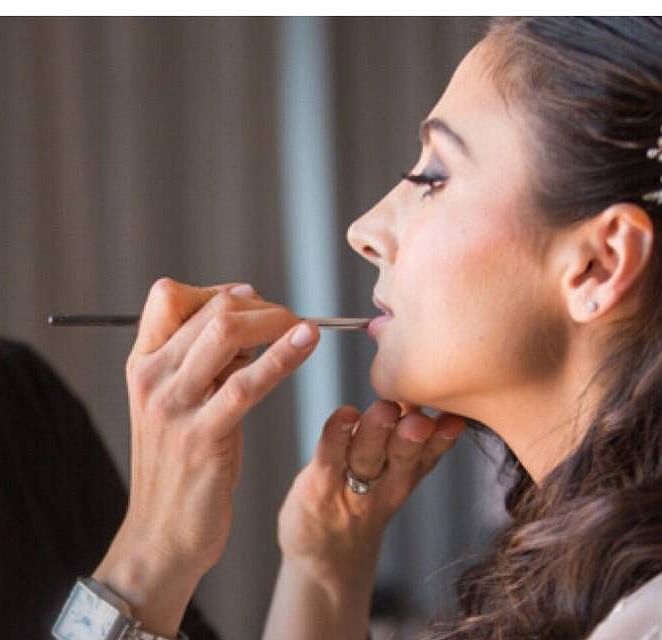 A woman applying makeup to another woman, gently brushing her lips with a makeup brush.