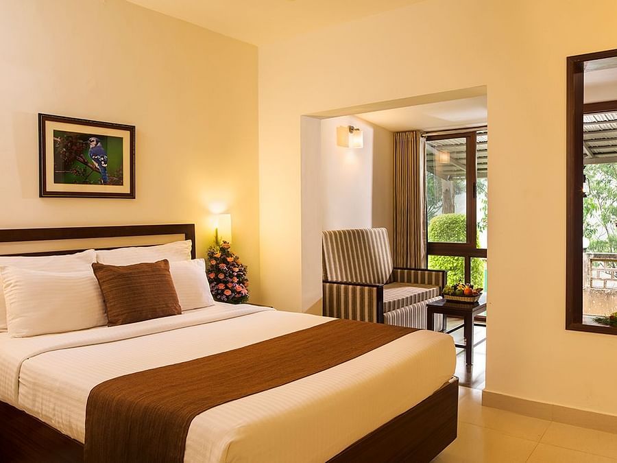 Room with a made-up bed, framed artwork hung on the wall, and a doorway leading to the balcony - Abad Copper Castle, Munnar