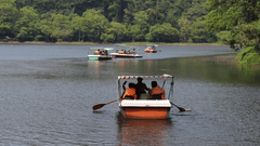 A row boat carrying people navigates a Pookode Lake, Wayanad, surrounded by trees.