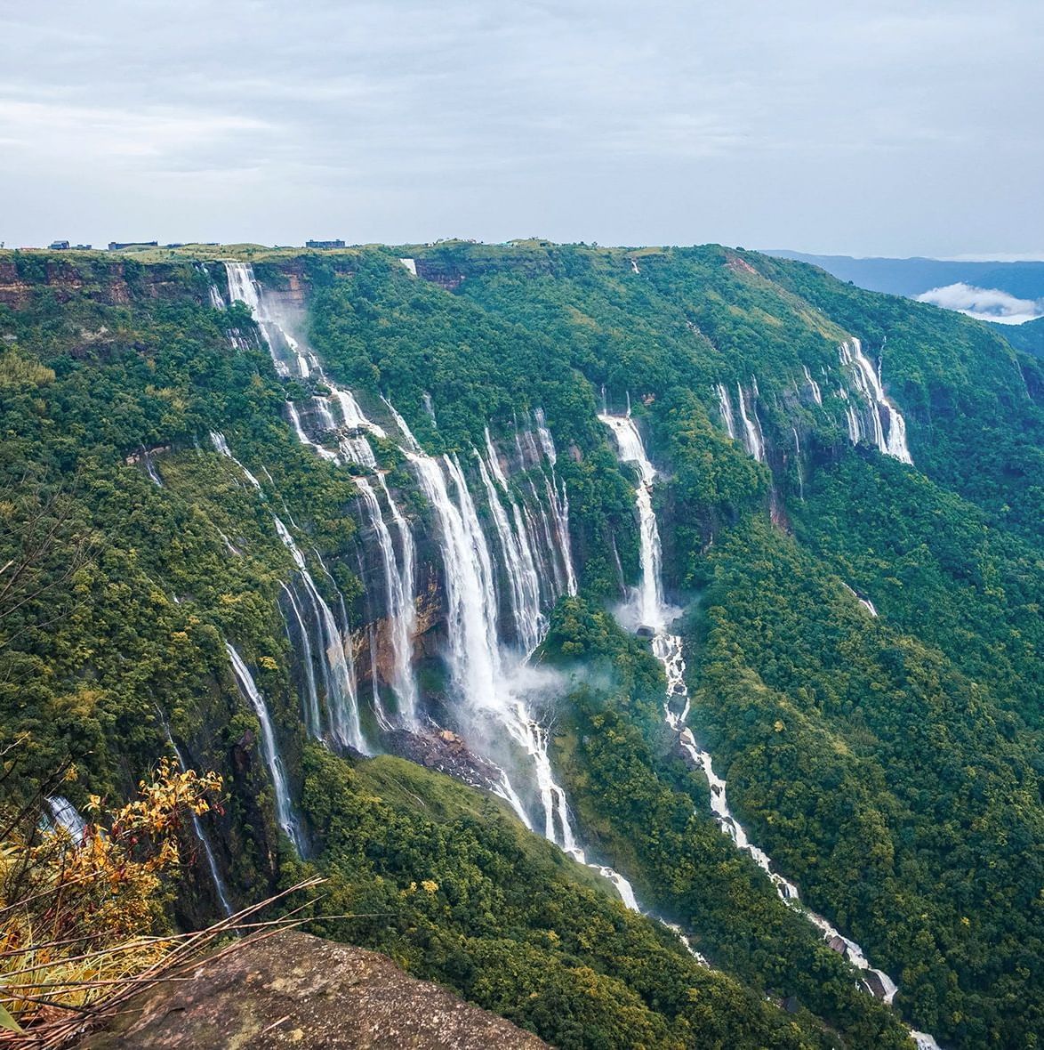 A wide view of a large waterfall with multiple streams flowing down a green cliff near Polo Resort Cherrapunjee.