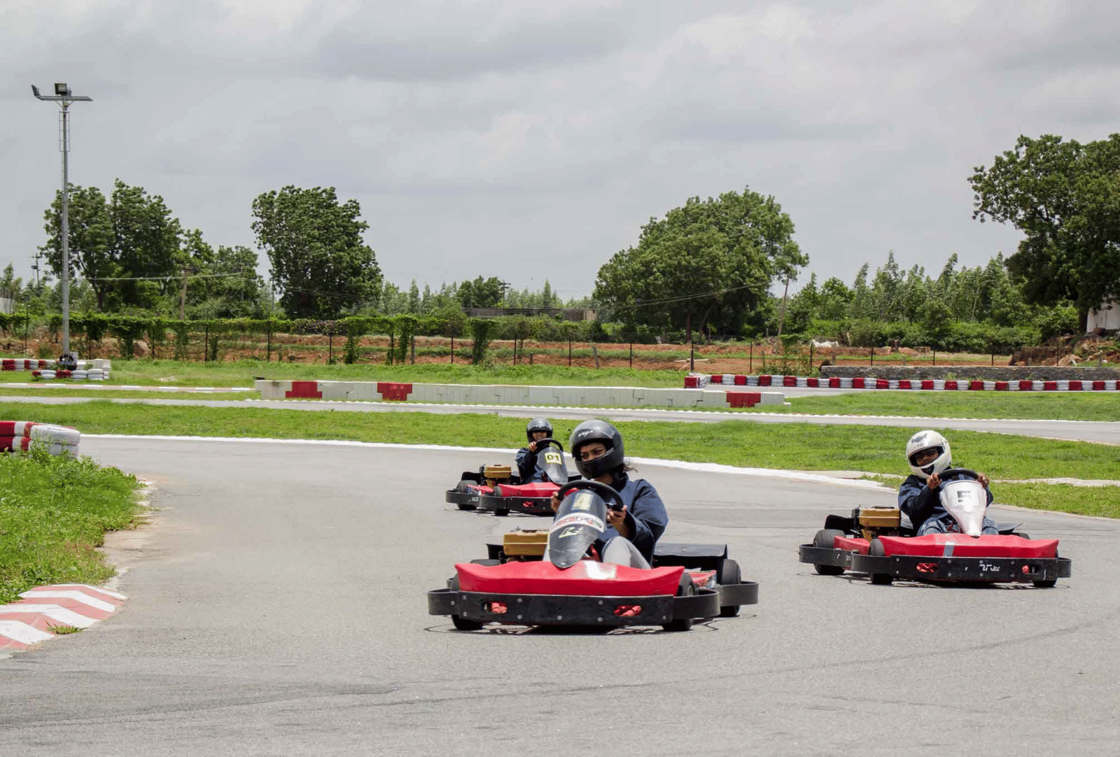 3 people enjoy racing go-karts around a curved outdoor track - District Gravity Adventure Park, Hyderabad