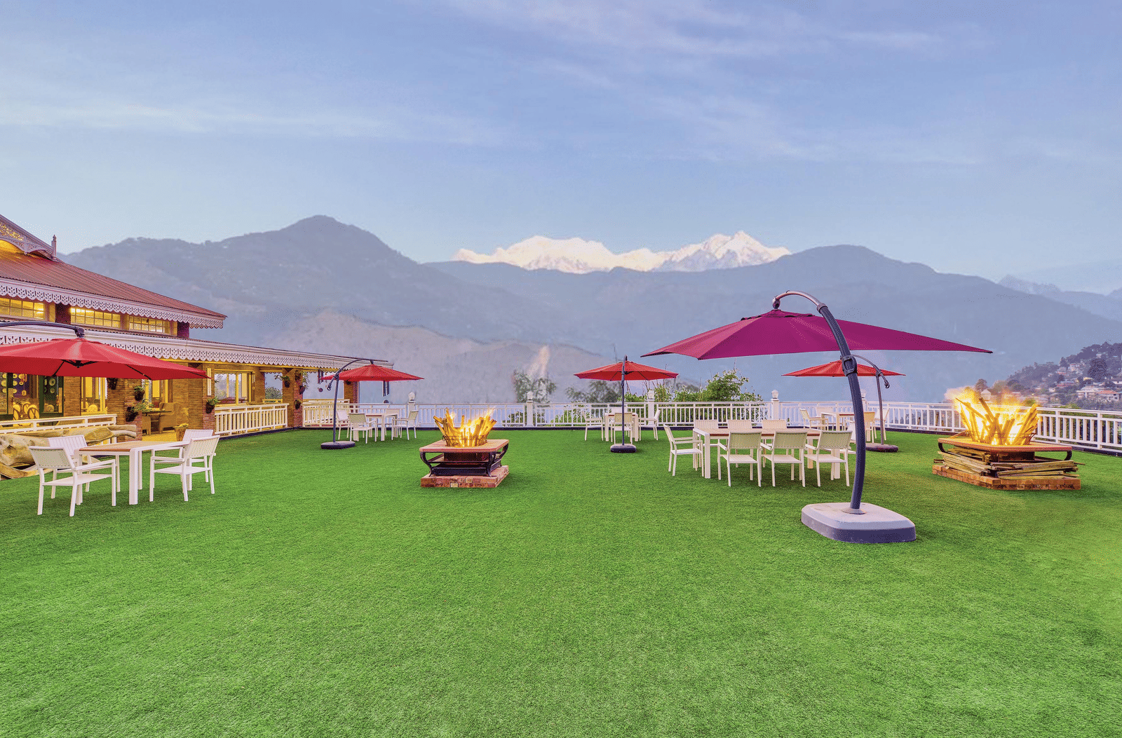 Open-air event lawn with dining tables, red parasols and lit fire pits, overlooking the snow-capped Kanchenjunga range at MAYFAIR Himalayan Spa Resort, Kalimpong.