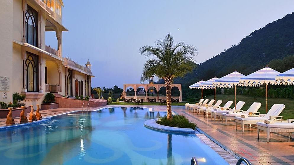 A swimming pool with seating area on the side and mountains in the background at Rajasthali Resort & Spa Jaipur.