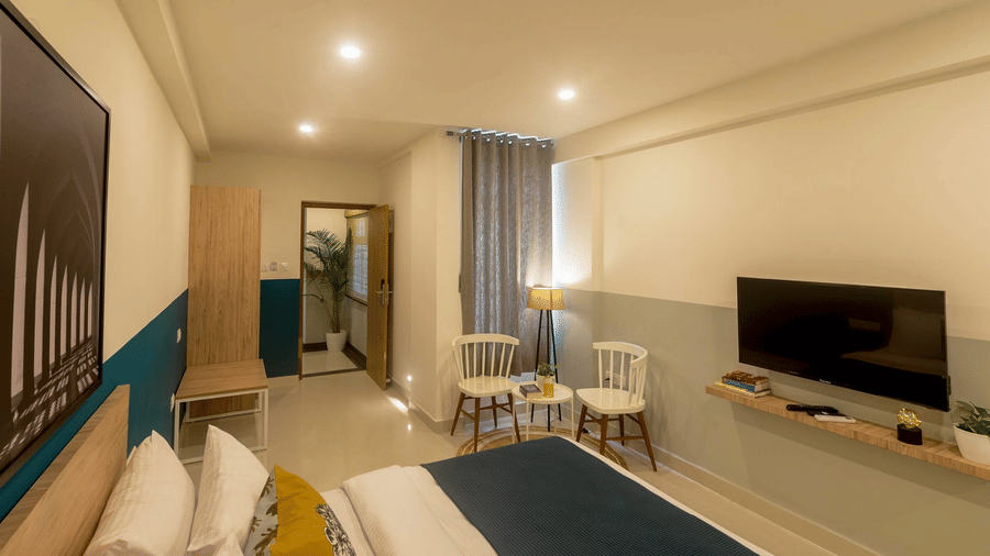 A perspective view of the hotel room from the bedside, looking toward the flat-screen TV and the entryway. The walls feature a two-tone teal and white paint design.