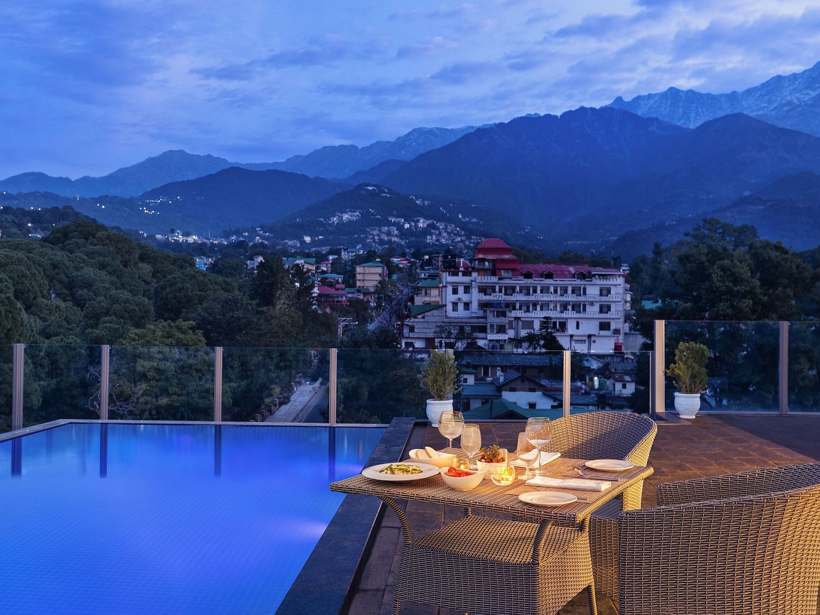 Rooftop pool lined with dining set up on the side on a clear blue day with mountains in the backdrop