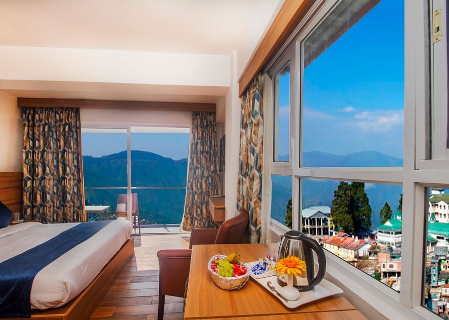 Cosy bedroom with large windows and a balcony overlooking scenic mountains, featuring a welcome tray with fruits and tea essentials - Central Heritage Resort and Spa