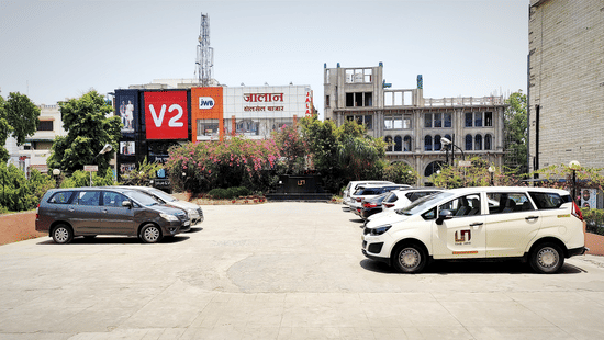 An outdoor parking lot with several cars parked in front of a multi-story building | HHI Varanasi