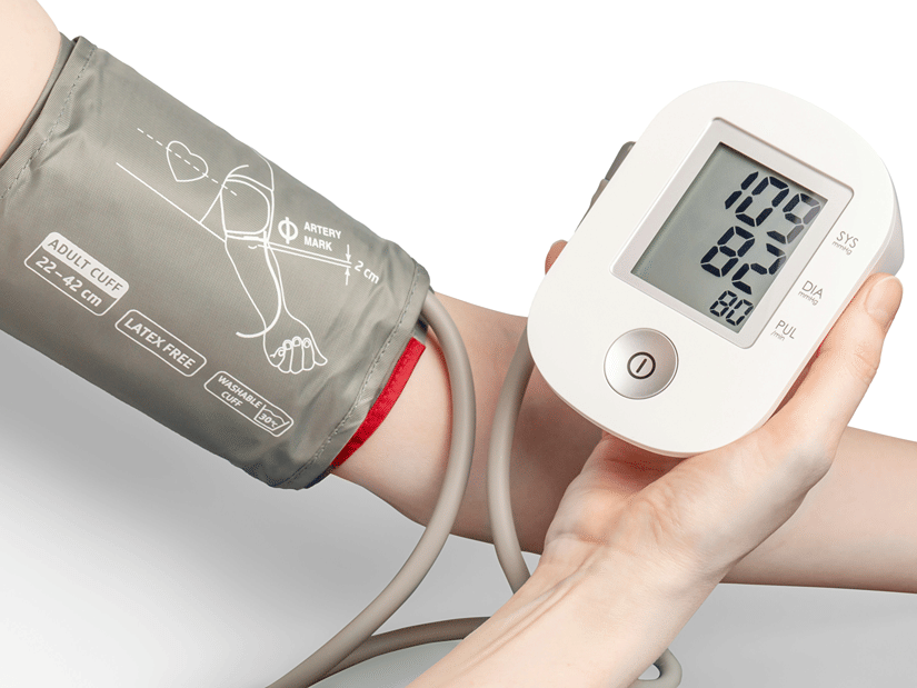 A digital blood pressure monitor held beside an arm wearing an inflatable cuff
