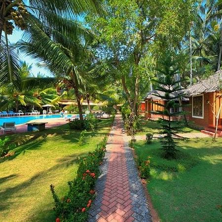 a pathway leading to the swimming pool and rooms next to many trees - Abad Harmonia, Kovalam