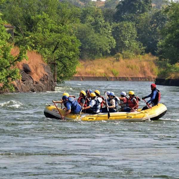 A group of people rafting on a flowing water body, while wearing safety devices, shot with the lush landscapes in the background.