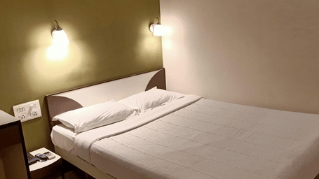 A Standard AC Room at Hotel Pandian, featuring a neatly-made bed with white sheets, 2 pillows, 2 wall lamps, and a nightstand.