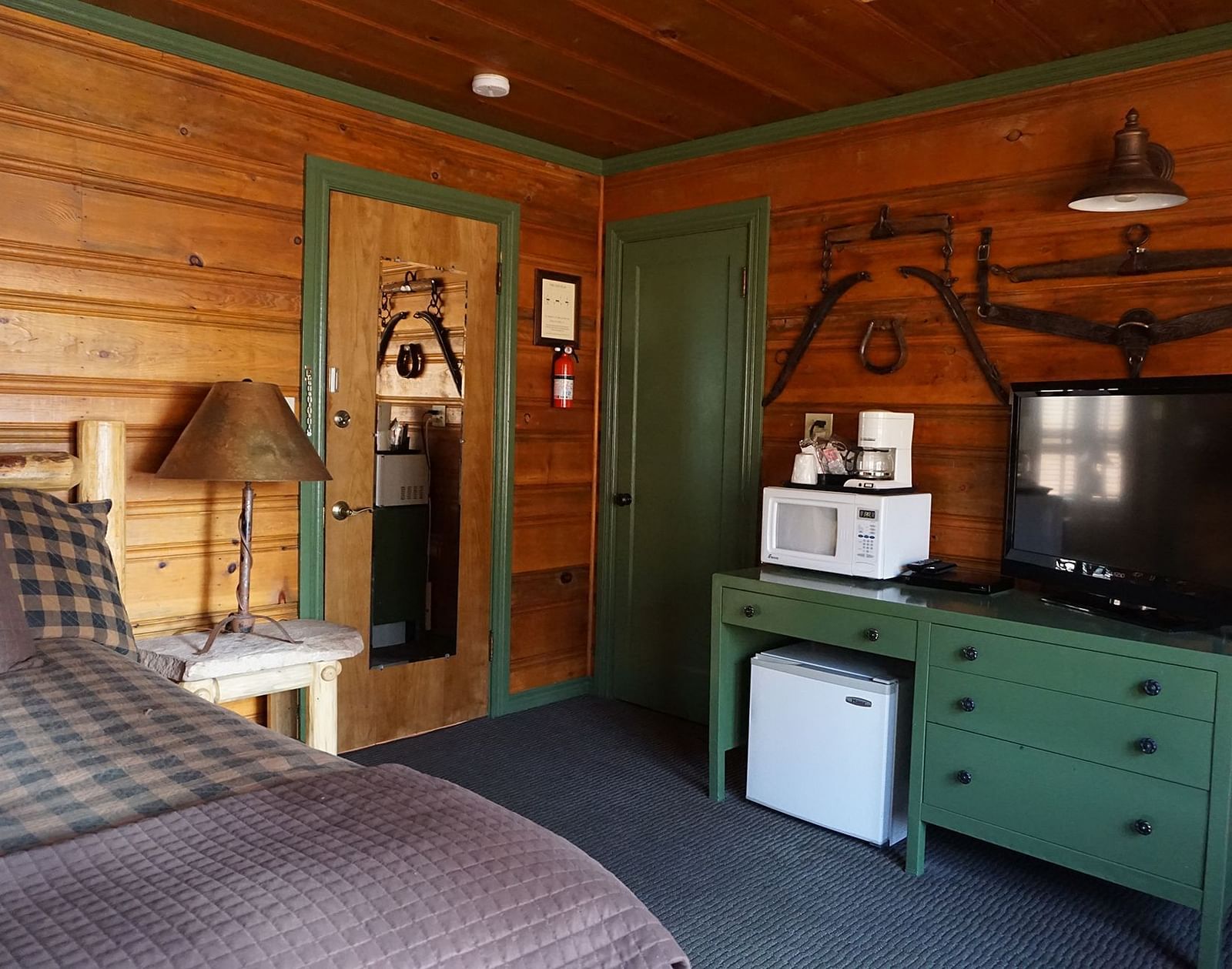 A room at Shaver Lake Village Hotel with a double bed, a lamp on a night stand, a green cabinet and wooden paneling throughout.