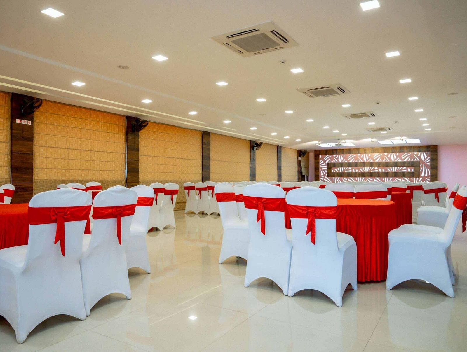 A large event space at Mansha Hotel Regency with numerous round tables covered in red tablecloths and white chairs.