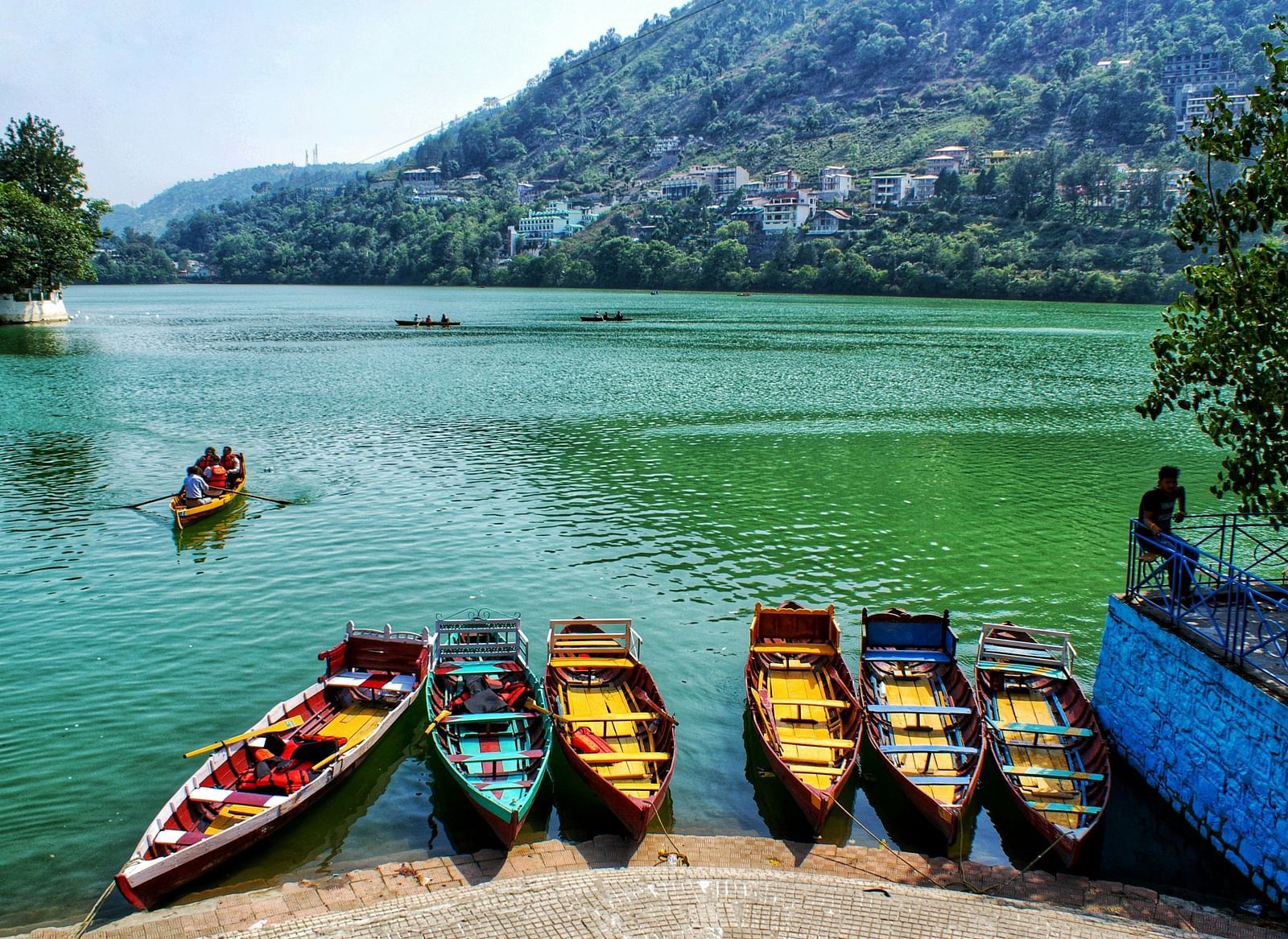 A row of colourful paddle boats lined up on the shore of a lake, with hills in the distance.