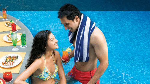 Two guests sitting poolside at the Sunken Bar in Mumbai at The Retreat Hotel and Convention Centre Madh Island, with a spread of dishes behind them.