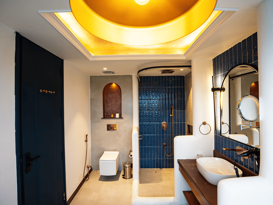 A bathroom layout with a wall-mounted toilet, a blue tiled shower enclosure, and a vanity counter at The Sierra - By The Lake.