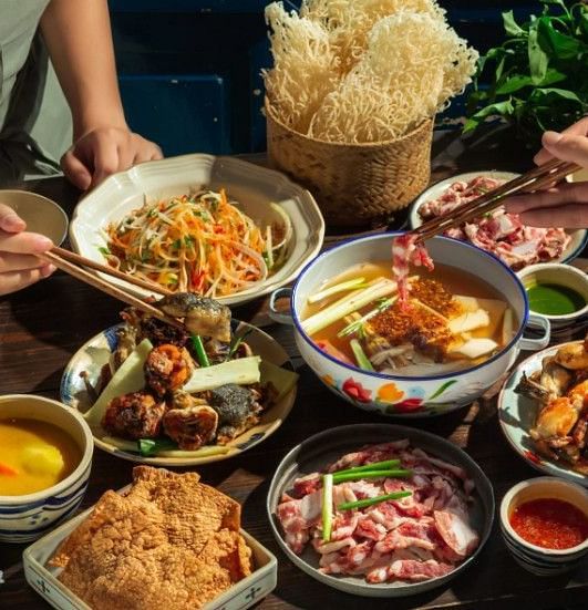 Close image of a dinner tale where various dishes are being enjoyed by people - Alibu Resort Nha Thrang
