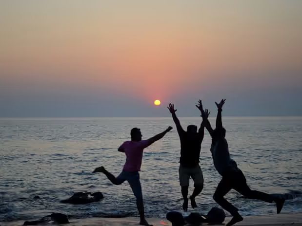 The silhouette of three children playing against a backdrop of a beach and a sunset.