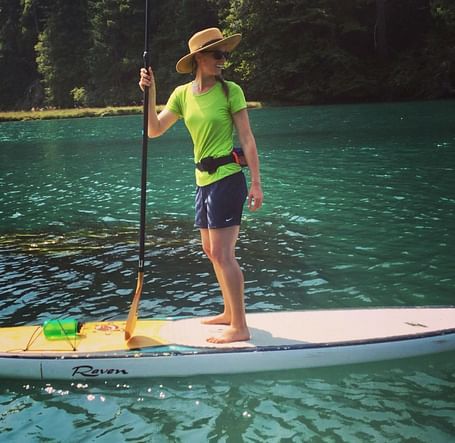 A person standing on a paddleboard in a calm body of water, holding a paddle.