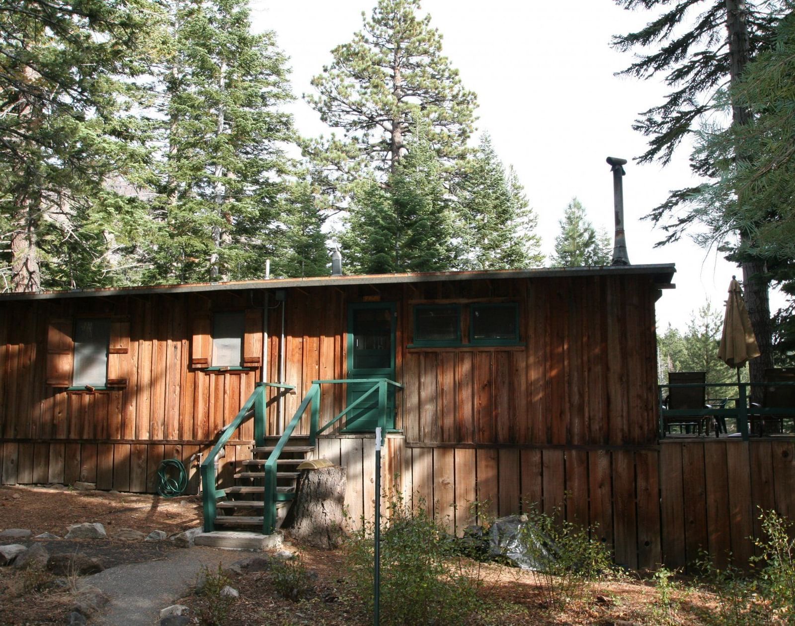 The side of a wooden cabin with a porch and steps leads down to a natural, forested area | Fawn