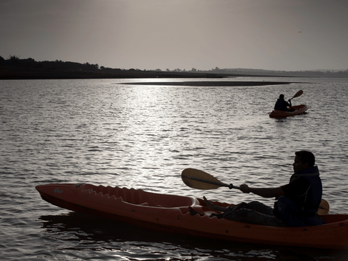 Kayaking In Kabini at The Serai featuring the silhouettes of a couple of people under a sunny sky