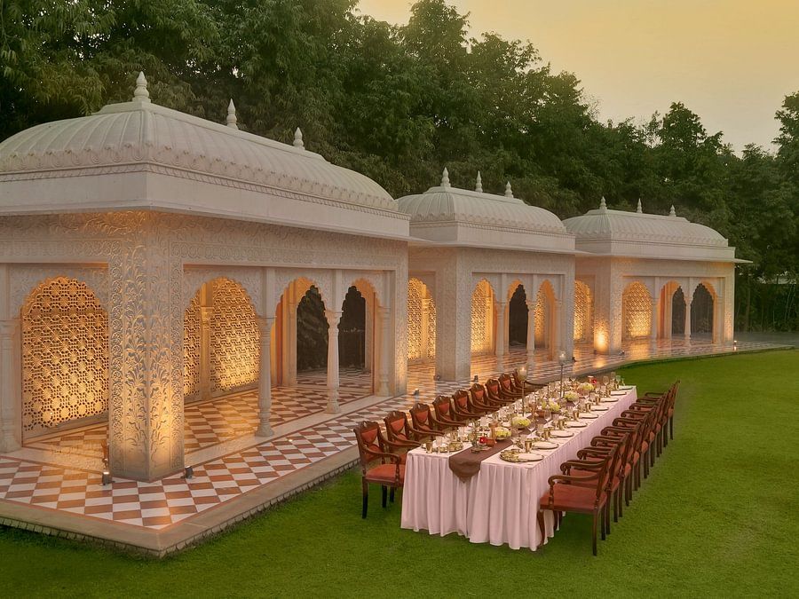Elegantly set long dining table under ornate, domed structures on a green lawn at dusk - Heritage Village Resorts & Spa.