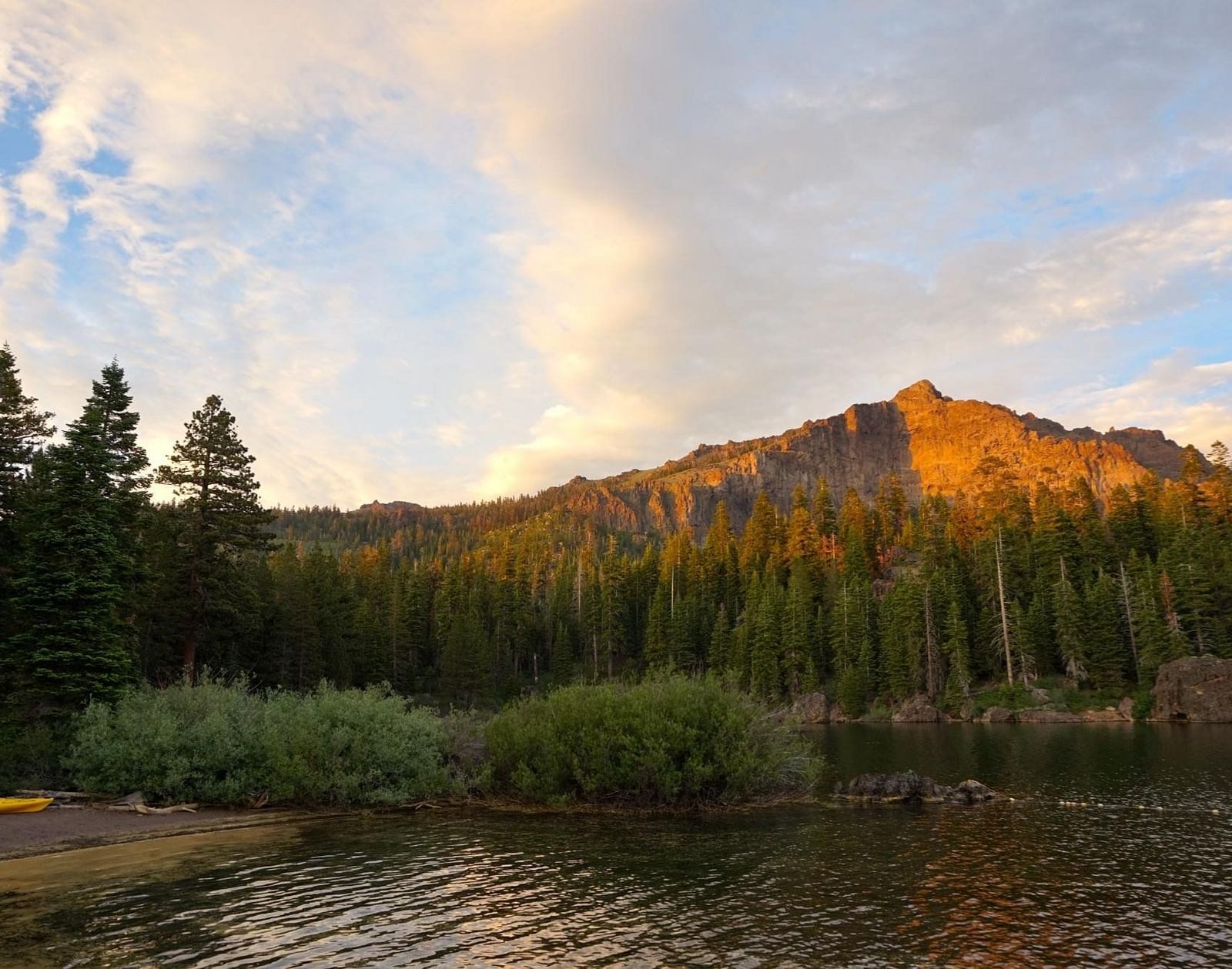 A sunset casts warm light on a mountain peak surrounded by a forest and a body of water
