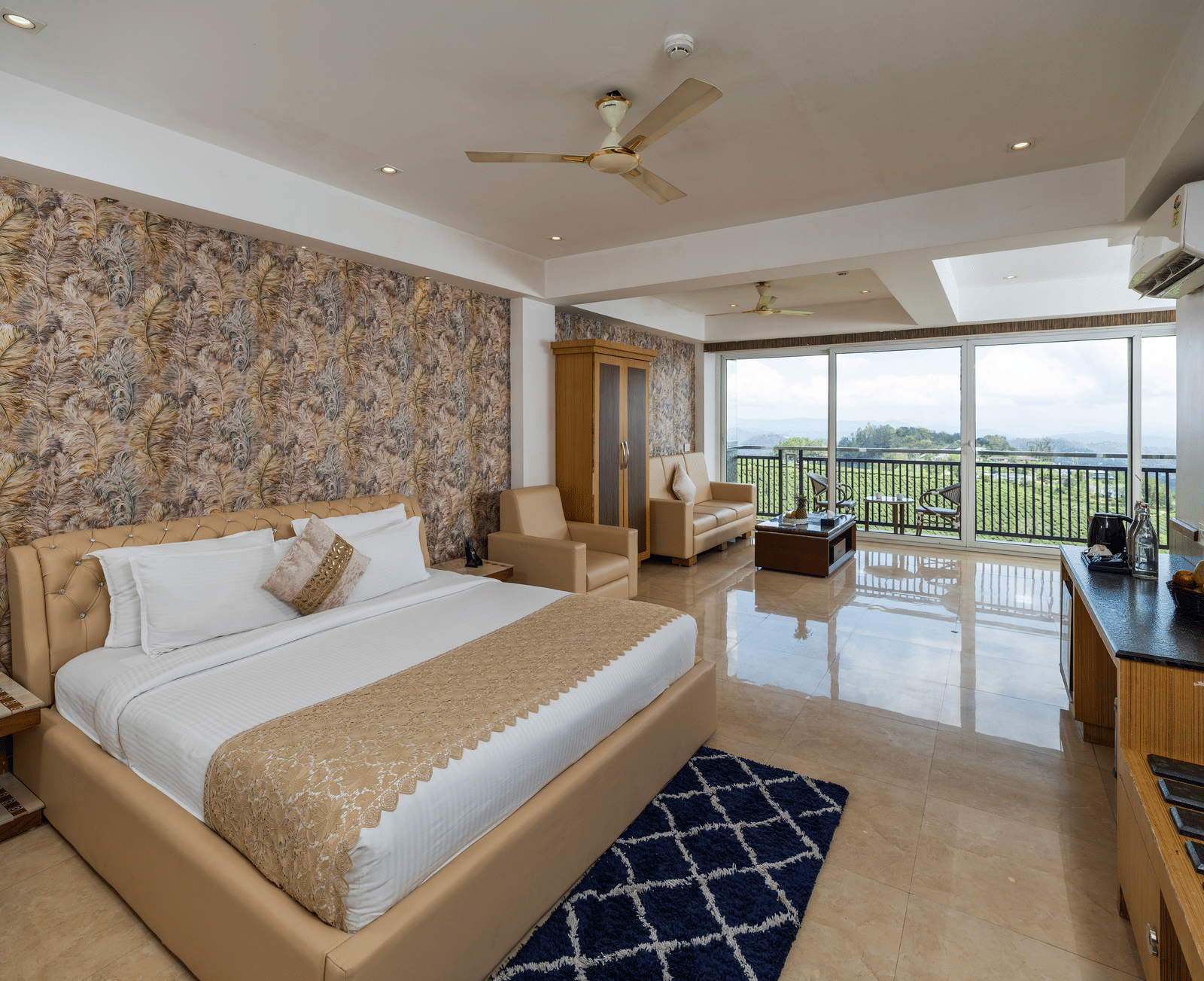 The bedroom of the 90-Degree Club Suite at Parakkat Nature Hotel and Resorts, Munnar, featuring a large bed, a stone-patterned accent wall, a ceiling fan, and glass windows.