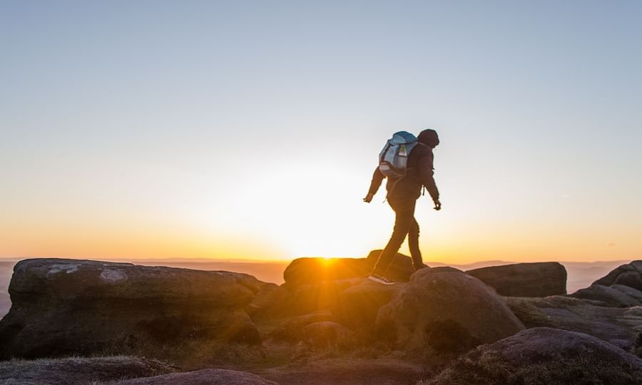 a person walking on rocks during his trek with the sun setting in the background